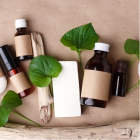 Naturalne produkty do pielęgnacji skóry z brązowymi etykietami, zielonymi liśćmi i kawałkami drewna wyrzuconego przez morze są ułożone na brązowym papierze. Scena ta oddaje ekologiczny, organiczny charakter produktów.